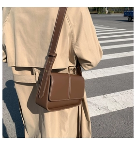 Detail of dark brown leather crossbody bag with topstitching worn over a trench coat