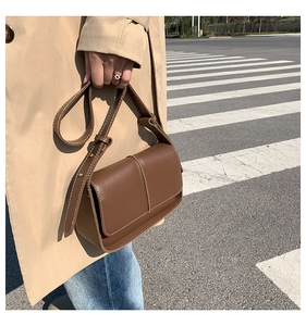 Detail view of brown vintage leather crossbody bag with contrast stitching on street