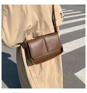 Detail view of brown leather crossbody bag with vertical stitching on urban background