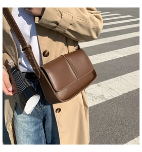 Brown retro leather crossbody bag styled with a beige trench coat for a city street look