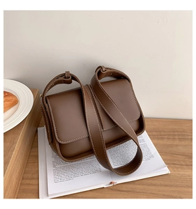 Close-up of brown faux leather crossbody bag with white stitching on wooden table