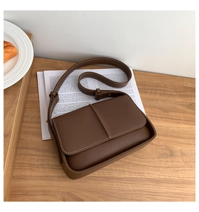 Close-up of retro brown shoulder bag with white contrast stitching on a wooden surface