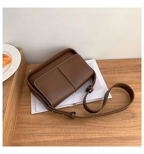 Detailed view of vintage brown leather crossbody bag with white contrast stitching on table