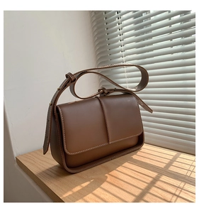 Detail of a brown leather shoulder bag featuring white contrast stitching on the window sill