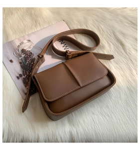 Detail of dark brown leather crossbody bag with white contrast stitching on soft white fur