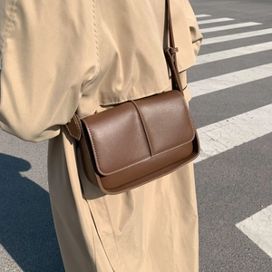 Elegant brown leather crossbody bag shown on a model in a minimalist street style scene