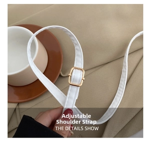 Detail showing the adjustable white leather shoulder strap with a golden square metal buckle