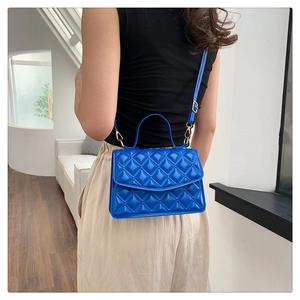 Detail of blue quilted pattern handbag with gold hardware and adjustable strap on a model