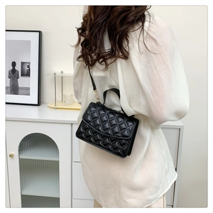 Detail of black quilted leather shoulder bag with gold metal buckles and refined stitching