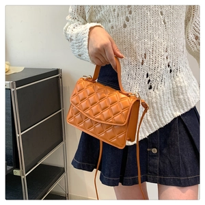 Detail of orange quilted crossbody bag with top handle and chain strap held by model