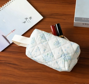 Close-up of white quilted makeup bag with blue floral print and fabric handle on wooden desk
