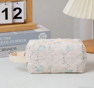 Detail of quilted floral makeup bag with blue petals and handle on a cozy desk setting