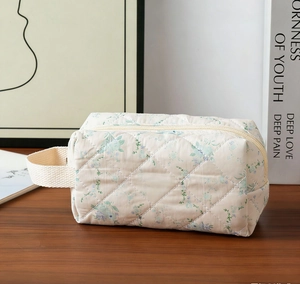 Detailed view of blue floral quilted makeup bag with side handle on a wooden table