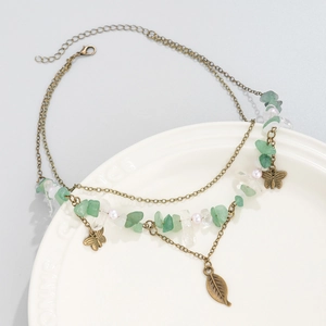 Detail view of retro bronze necklace with green stones, pearls, and butterfly charms