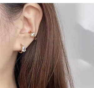 Detail of gold drip earring and rectangular cuff set with zircon stones on ear