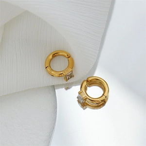 Detail of gold huggie hoop earrings with square cubic zirconia on white silk background