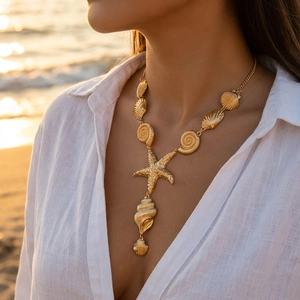 Close-up of golden starfish and seashell pendant necklace on model at sunset beach