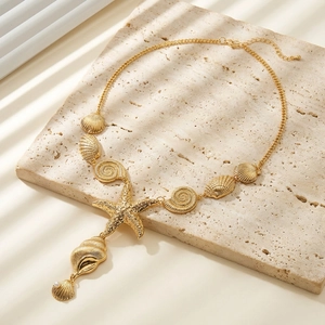 Golden starfish and seashell necklace with pearl on stone tray under aesthetic window shadow