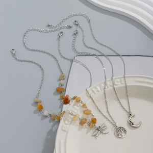 Detail of silver necklaces with dragonfly, tree of life, and moon pendants on white plate