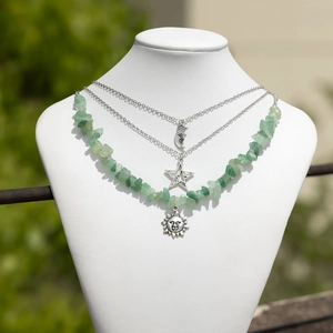 Detailed close-up of a triple-layered necklace with green stones and celestial pendants