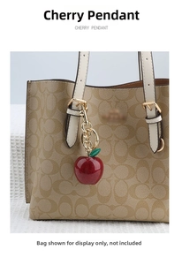 Detailed view of a shiny red cherry pendant on a handbag with a golden key chain