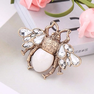 Vintage gold bee brooch with rhinestones and white bead on a classic book background