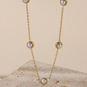Elegant minimalist gold chain necklace with round white pearls on a natural stone base