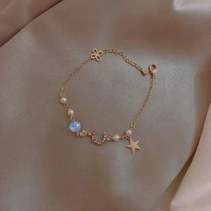 Goldenes Armband mit Stern-, Mondanhängern, blauer Perle und Perlen auf Champagner-Satin