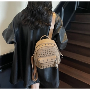Detail view of khaki rivet studded soft leather backpack worn by model on stairs