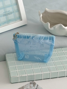 Detail of blue mesh cosmetic bag featuring shell embroidery and a gold star charm zipper