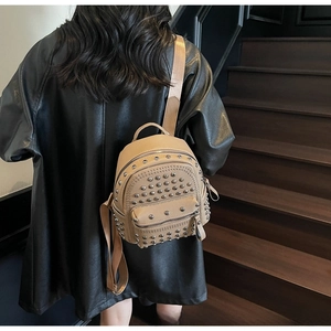 Detail of khaki pebbled leather backpack with silver studs worn by a model on stairs