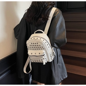 Close-up of a white leather backpack with silver rivets worn over a black coat