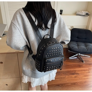 Detail of a black leather mini backpack with silver rivets shown on a model's back