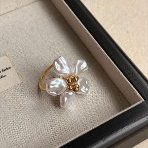 Makroaufnahme eines Barock-Perlenblumenrings mit goldenem Kern auf beigem Leinen