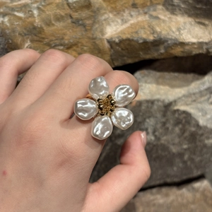 Detailansicht eines Blumenrings aus Gold mit Perlenblütenblättern am Finger