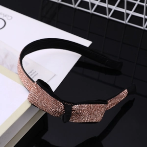 Dettaglio del cerchietto con strass oro rosa e fiocco elegante su tessuto nero