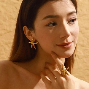 Close-up of a model wearing gold starfish stud earrings and a matching open ring