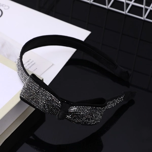 Dettaglio di un cerchietto sottile nero con fiocco di strass scintillanti su base lucida