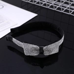 Dettaglio di cerchietto nero con fiocco e strass su una superficie riflettente