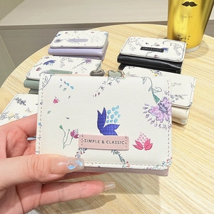 Detail of floral trifold short wallet featuring a pink label and metal heart clasp
