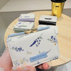 Close-up of a floral print tri-fold wallet featuring a gold heart clasp and leather label