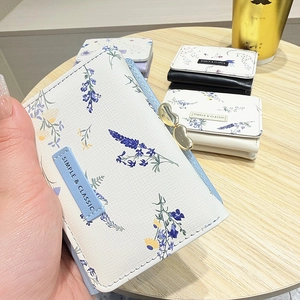 Detail of a white floral tri-fold wallet with a gold heart clasp and PU leather texture