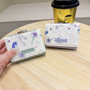 Floral tri-fold wallets in pastel colors with heart-shaped metal clasps on wood table