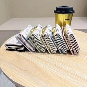 Multiple mini floral bifold wallets with metal clasps displayed on a wooden table