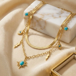 Detail of double-layer gold snake chain with evil eye and starburst pendants on marble