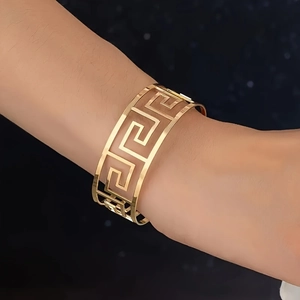 Detailed view of wide gold cuff bracelet featuring classic Greek key hollow patterns