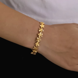 Detailed view of golden flower bracelet with textured petals on a model's wrist