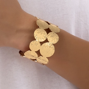 Detailed close-up of wide golden cuff bracelet with hammered circular plate textures