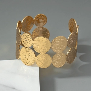 Macro detail of golden wide hammered texture cuff bracelet on a marble stone base
