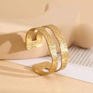 Detail of wide gold cuff bracelet featuring hollow layers and hammered lava texture